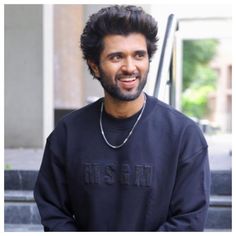 a man in a black sweatshirt is standing outside with his hands in his pockets and smiling at the camera