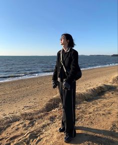 a woman standing on top of a sandy beach next to the ocean with her eyes closed