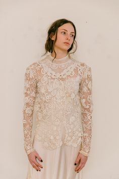 a woman standing in front of a white wall wearing a long sleeved top and skirt