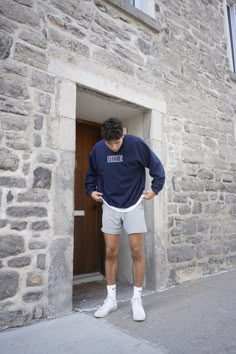 a young man standing in front of a door wearing shorts and a blue sweatshirt with the word brooklyn on it