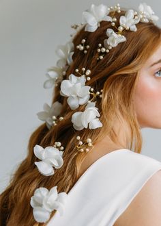 a woman with long red hair wearing a white dress and flowers in her hair is looking off to the side