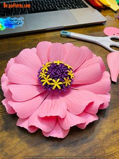 a pink flower sitting on top of a wooden table next to a laptop computer and scissors