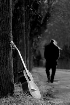 a guitar leaning against a tree on the side of a road with a man walking by