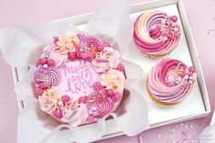 two cupcakes with pink frosting and flowers on top in a white box