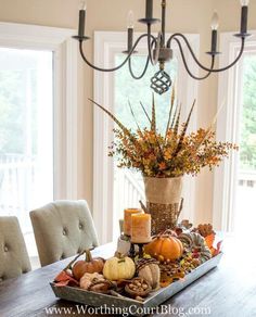 a dining room table decorated for fall with candles and pumpkins