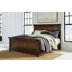 a bed with a wooden frame and headboard in front of two windows on a rug