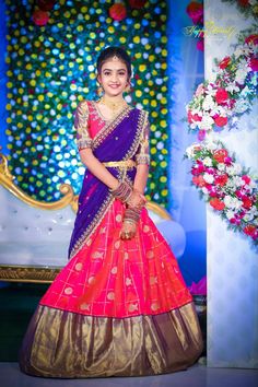 a woman in a purple and pink lehenga standing next to a flower arrangement