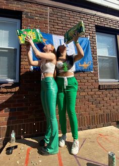 two women in green pants standing next to each other near a brick building with windows