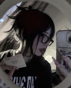 a woman with glasses is looking at her cell phone and holding a paper in front of her face