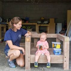 a woman kneeling down next to a toddler sitting on a wooden bench in a garage