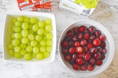 grapes and cherries in bowls next to cartons of yogurt on a marble counter