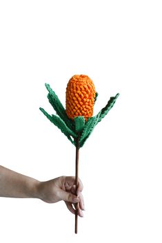 a hand holding a flower made out of knitted yarn on a stick with leaves