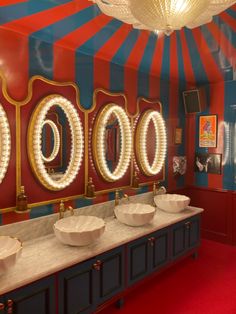 a bathroom with two sinks and three mirrors on the wall, in front of a circus theme