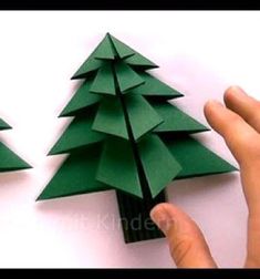 someone is cutting out paper christmas trees with their fingers and pointing to the one on the other side