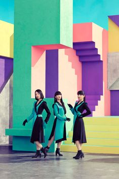 three young women standing in front of a colorful wall with stairs and steps behind them