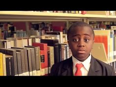 a boy in a suit and tie standing in front of bookshelves with his eyes wide open