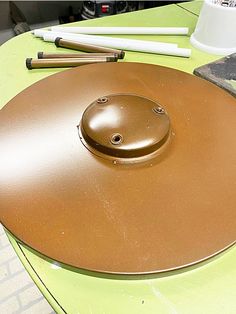 a round metal object sitting on top of a green table next to some pencils