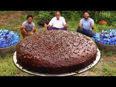 three men sitting in front of a large chocolate cake