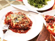 a white plate topped with lasagna covered in sauce and cheese next to a salad