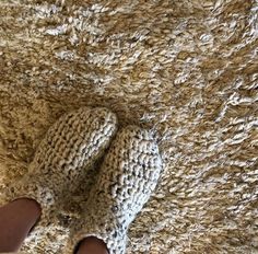 someone's feet in knitted slippers laying on a shaggy brown area rug