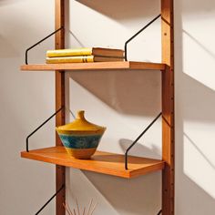 a yellow vase sitting on top of a wooden shelf next to two bookshelves