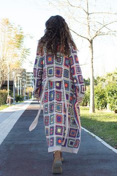 a woman is walking down the street wearing a colorful crochet coat and boots