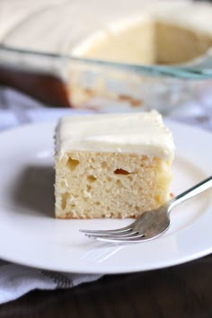 a piece of cake on a white plate with a fork next to it and a glass dish in the background