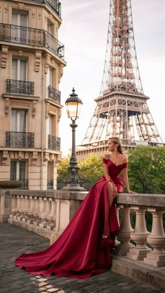 a woman in a red dress sitting on a ledge near the eiffel tower