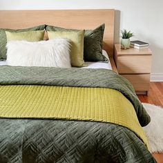 a bed with green and yellow pillows on top of it next to a night stand