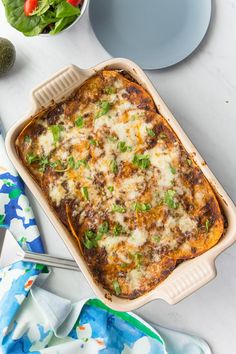 a casserole dish with cheese and vegetables in it on a white table next to other dishes