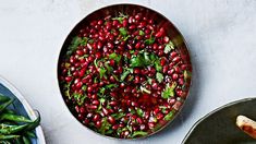 pomegranates in a bowl next to green beans and other food items