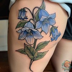 a woman's thigh with blue flowers and green leaves on the side, in front of her