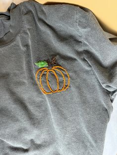 Hand embroidered pumpkin on a super cozy Comfort Colors Pepper colored Tee.  Sizes run unisex. Cheap Custom Embroidered Tops For Fall, Black T-shirt With Custom Embroidery For Fall, Custom Embroidery Relaxed Fit T-shirt For Fall, Embroidered Black T-shirt For Fall, Casual Embroidered Fall T-shirt, Embroidered Relaxed Fit T-shirt For Fall, Casual Embroidered T-shirt For Fall, Casual Tops With Custom Embroidery For Fall, Fall Cotton T-shirt With Embroidered Graphics