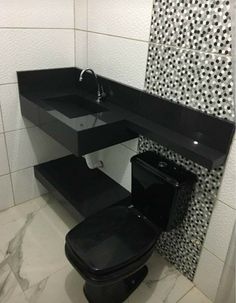 a black toilet sitting next to a sink in a bathroom with tiled walls and floor