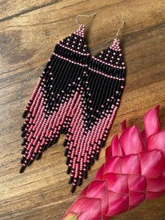 pink and black seed beaded earrings on wooden table next to red flower with petals