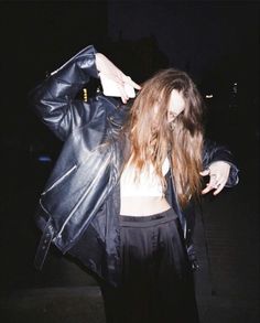 a woman with long hair wearing a black leather jacket and holding her hand on her hip