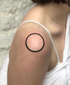 a woman's arm with a black circle tattoo on the back of her shoulder