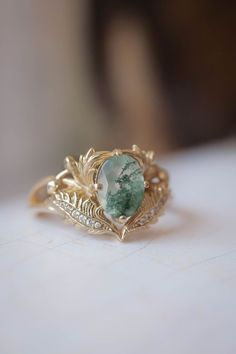 a close up of a ring with a green stone on the center and leaves around it