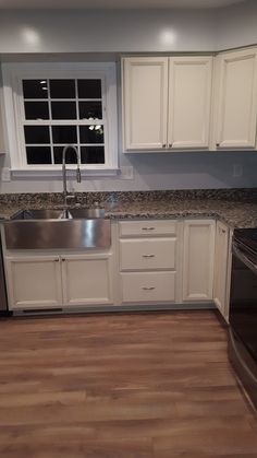 an empty kitchen with stainless steel appliances and white cabinets, wood floors, and a window