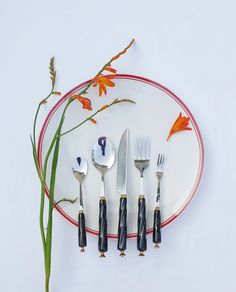 there is a plate with five forks and six spoons next to flowers on it