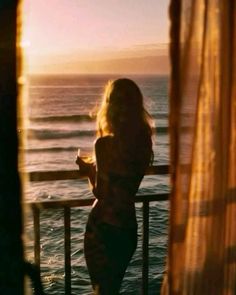 a woman standing on a balcony next to the ocean