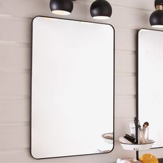 two mirrors are hanging on the wall in front of a sink and mirror with lights above it