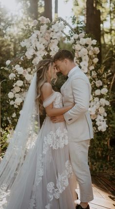 a bride and groom standing in front of a floral arch