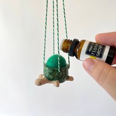 a hand holding an essential oil bottle next to a tiny turtle on a string necklace