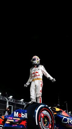 a man standing on top of a red and white race car in front of a black background