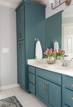 a bathroom with blue cabinets and flowers in the vase on the sink counter top, along with an area rug