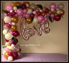 a balloon arch with the word love spelled out in pink, white and gold balloons