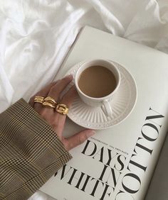 a person's hand on top of a book with a cup of coffee in front of them