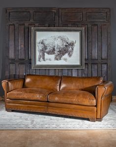 a brown leather couch sitting in front of a wooden paneled wall with a buffalo drawing on it