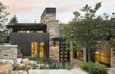 a modern home with stone and brick exterior, surrounded by trees and flowers in the foreground